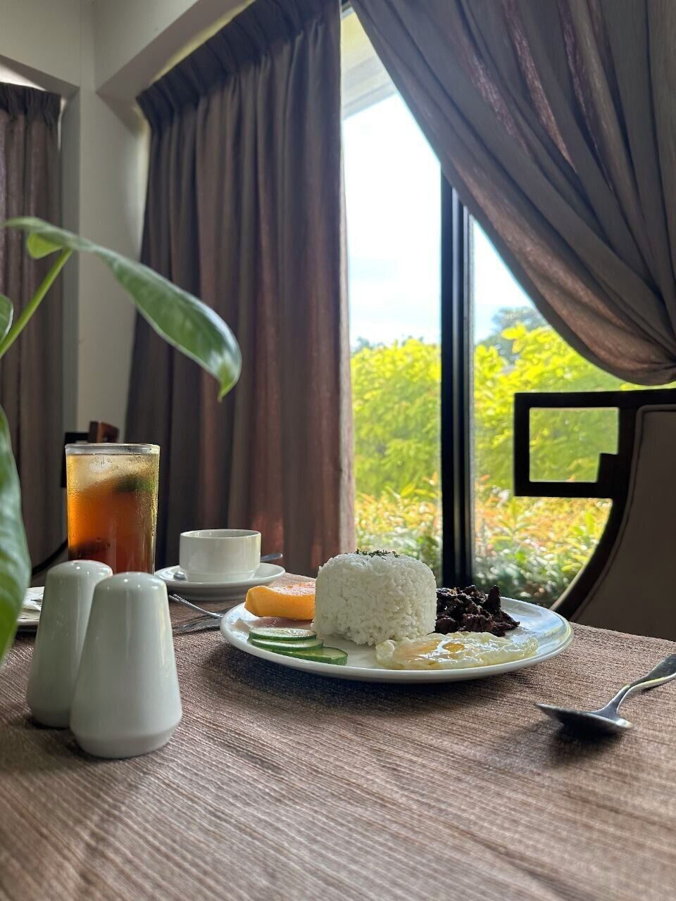 Una mesa de comedor con un plato de comida, un vaso de té helado y saleros y pimenteros.