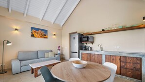 A modern living room with a sofa, a dining table with chairs, a kitchen area with a microwave, and a painting on the wall. - Kura Kabana by Boutique Bonaire Unique Resorts (Kralendijk)
