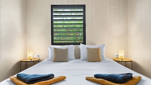 A hotel room with a large bed, two bedside tables with lamps, a window with blinds, and a view of greenery outside. - Kura Kabana by Boutique Bonaire Unique Resorts (Kralendijk)