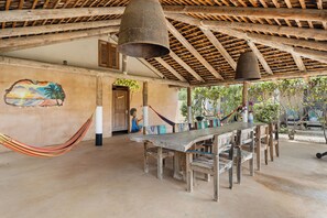 Un espace de restauration extérieur rustique, avec une table et des bancs en bois, un hamac et une fresque murale.