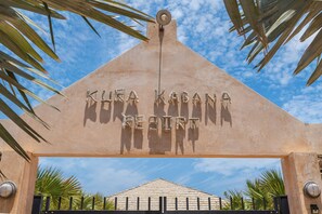 Une enseigne sur laquelle on peut lire « KUEA KABANA RESORT », entourée de palmiers et surplombant un ciel dégagé.