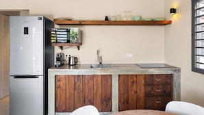 A kitchen with a built-in refrigerator, wooden cabinets, a countertop, and a shelf with glassware. - Kura Kabana by Boutique Bonaire Unique Resorts (Kralendijk)