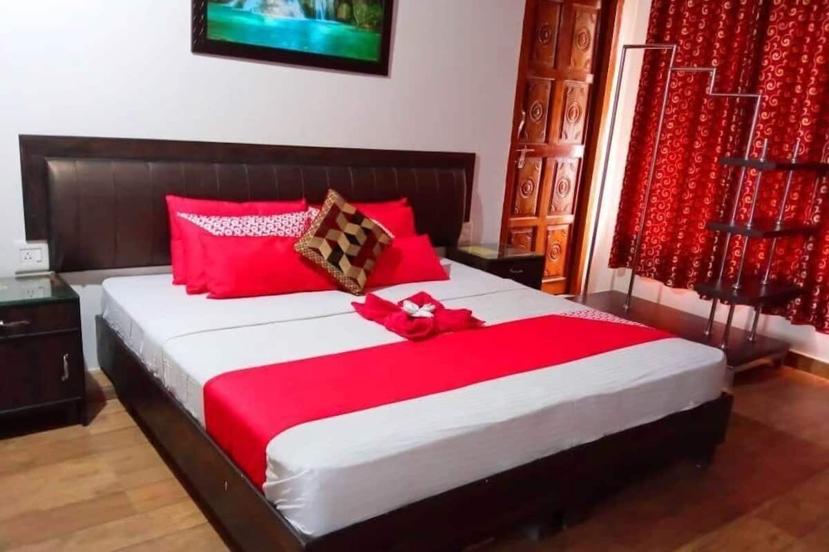 Un lit bien fait, avec une literie rouge et blanche, une tête de lit en bois, une table de chevet avec une lampe et un rideau rouge.