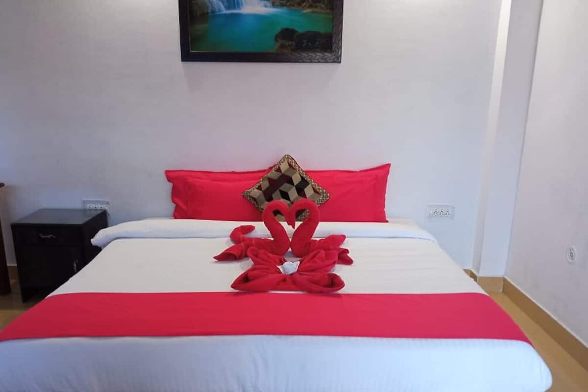 Une chambre d’hôtel avec un lit, une couvre-lit rouge et blanche, un oreiller rouge et un tableau représentant une cascade accroché au mur.
