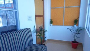 Una habitación con un sofá a rayas, dos plantas en macetas y una ventana con persiana de madera.