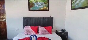A bedroom with a bed, two red patterned pillows, a nightstand with a phone, and a wall-mounted picture of a waterfall. - Hotel Sheetal Tower (Lansdowne)