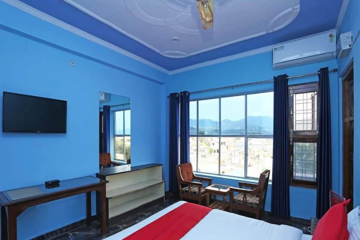 Une chambre d’hôtel équipée d’un lit, d’un bureau, d’une chaise, d’une télévision et d’une grande fenêtre donnant sur un paysage agréable.