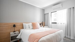 A modern hotel room with a large bed, a nightstand, a lamp, and a view of the city through the window. - Charlie Jerônimo da Veiga (São Paulo)