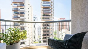 A balcony with a potted plant and a chair, overlooking tall residential buildings. - Charlie Jerônimo da Veiga (São Paulo)