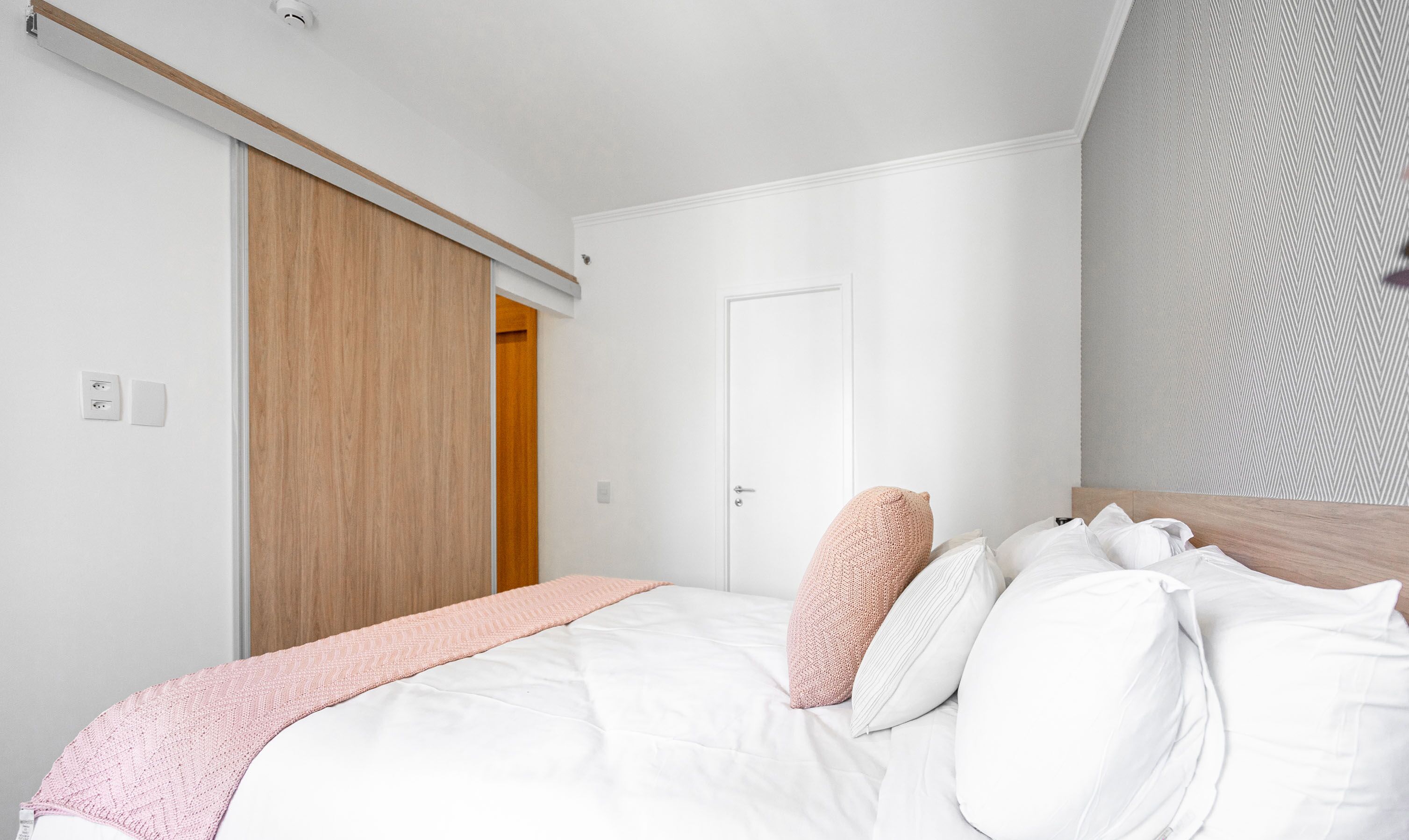 A bedroom with a bed, a wooden wardrobe, a white door, and a patterned wall.