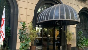 A hotel entrance with a large arched doorway, potted plants, and a flag. - Charlie Jerônimo da Veiga (São Paulo)