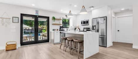 A modern kitchen with white cabinetry, stainless steel appliances, and a central island with stools.