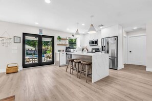 A modern kitchen with white cabinetry, stainless steel appliances, and a central island with stools. - Coco Loco, tropical pool oasis near beach (Deerfield Beach)