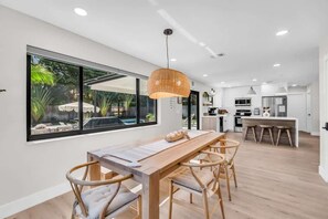Une cuisine moderne dotée d’un grand îlot central, d’un coin repas avec une table et des chaises en bois, et d’une grande fenêtre donnant sur un jardin.