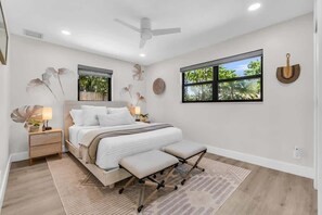 Une chambre moderne avec un lit, des tables de chevet, un ventilateur de plafond et une fenêtre donnant sur un paysage verdoyant.
