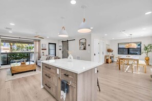 Een moderne keuken met een centraal eiland, hanglampen en een eethoek met een tafel en stoelen.