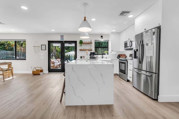 A modern kitchen with a marble island, stainless steel appliances, and a dining area with a wooden table and chairs.