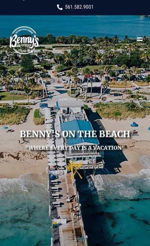 An aerial view of a beachside resort with a pier, beach umbrellas, and lounge chairs.