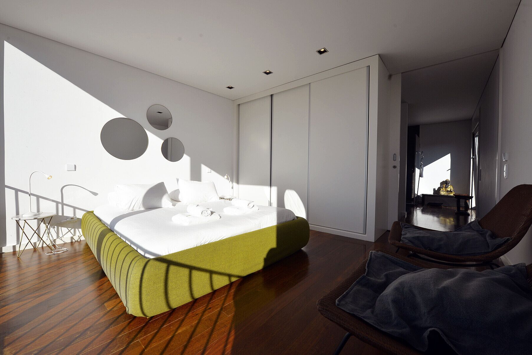 Une chambre moderne avec un grand lit, un coin salon avec un fauteuil et une armoire.