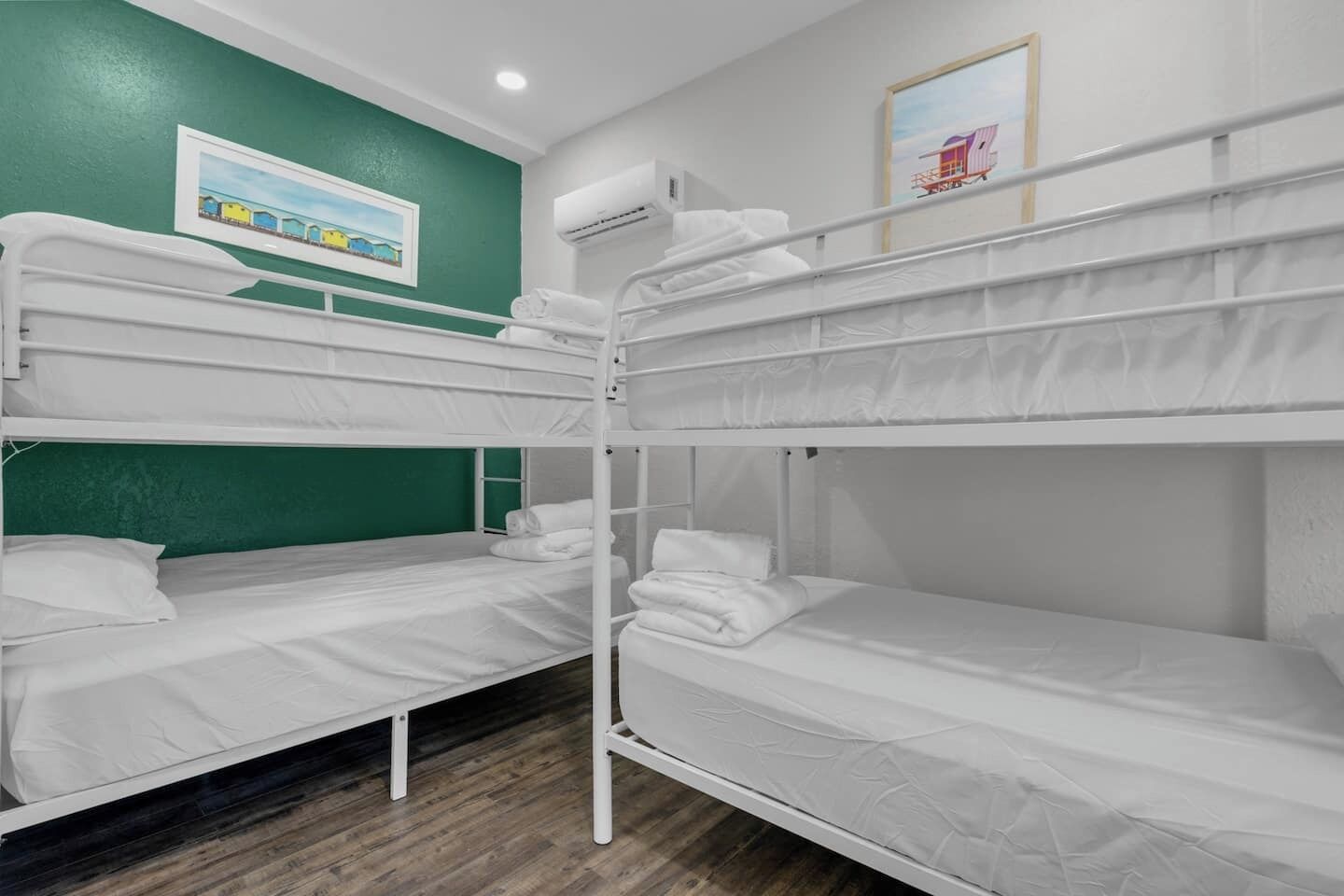 A bunk bed room with white bedding, a green accent wall, and a framed picture above the beds.