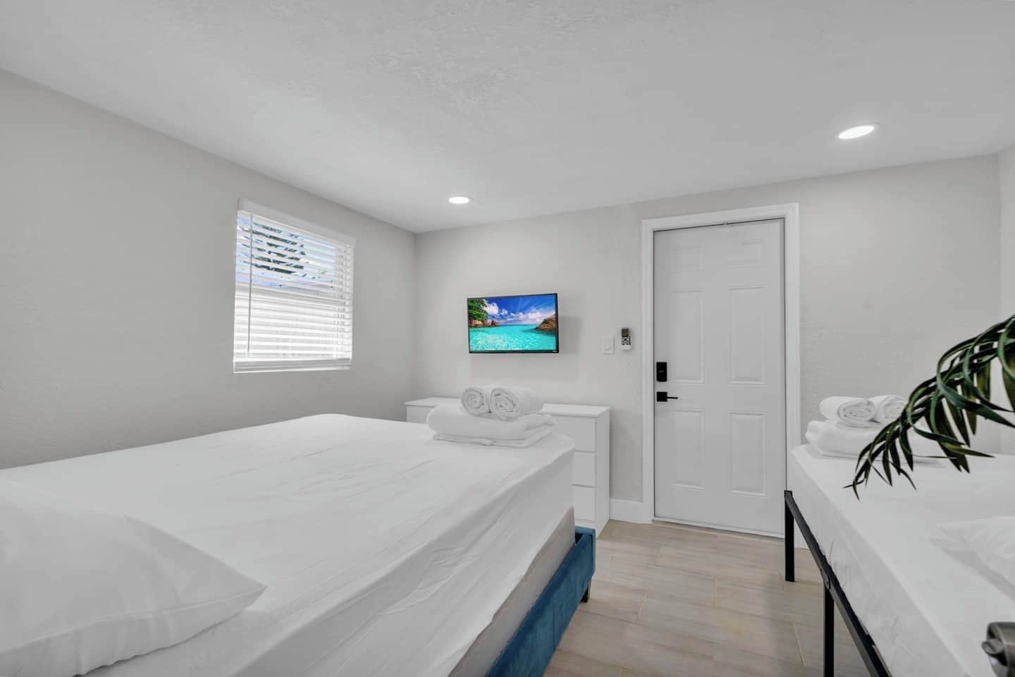 A modern hotel room with a single bed, a TV mounted on the wall, and a door leading to the bathroom.