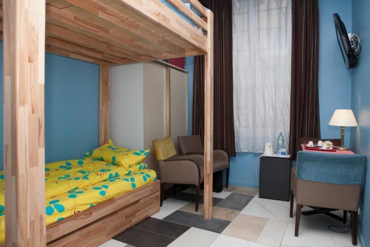 A room with a bunk bed, a chair, a small table with a lamp, and a wall-mounted phone.