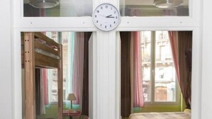 Una habitació amb un llit, una taula de treball i una cadira. Hi ha un rellotge a la paret.
