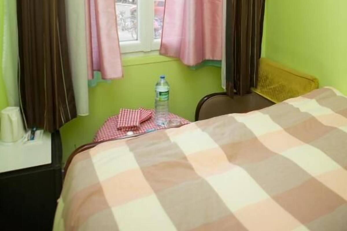 A room with a bed, a television, a window with curtains, and a bottle of water on a small table.