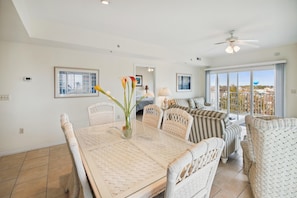 A spacious living area with a dining table, wicker furniture, and a balcony with a view. - XPLORIE ACTIVITIES & LINENS INCLUDED*! Great 3BR Condo Just a Short Walk to the Beach, Dining & Activities! (Ocean City)