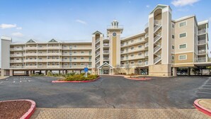 A multi-story hotel with a central tower, a parking lot, and a landscaped entrance area.