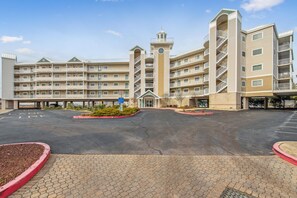 A multi-story hotel with a central tower, a parking lot, and a landscaped entrance area.
