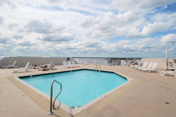A rooftop pool with white lounge chairs and a clear blue sky.