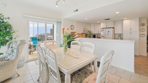 A modern kitchen with white cabinets, a central island, and a dining area with wicker chairs and a glass table.