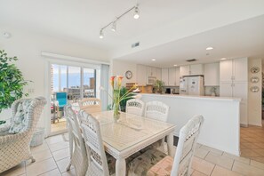 A modern kitchen with white cabinets, a central island, and a dining area with wicker chairs and a glass table.
