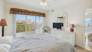 A hotel room with a bed, a television, a dresser, and a balcony with a view of the city.
