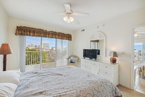 A hotel room with a bed, a television, a dresser, and a balcony with a view of the city.