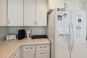 Una kitchenette con un refrigerador blanco, una cafetera, un tostador y una tetera eléctrica negra.