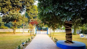 A pathway leading to a gated entrance surrounded by trees and a white picket fence. - Mykonos Villa (Varanasi)