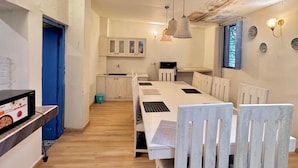 A spacious kitchen with a long dining table and chairs, a blue door, and a microwave on the counter. - Mykonos Villa (Varanasi)