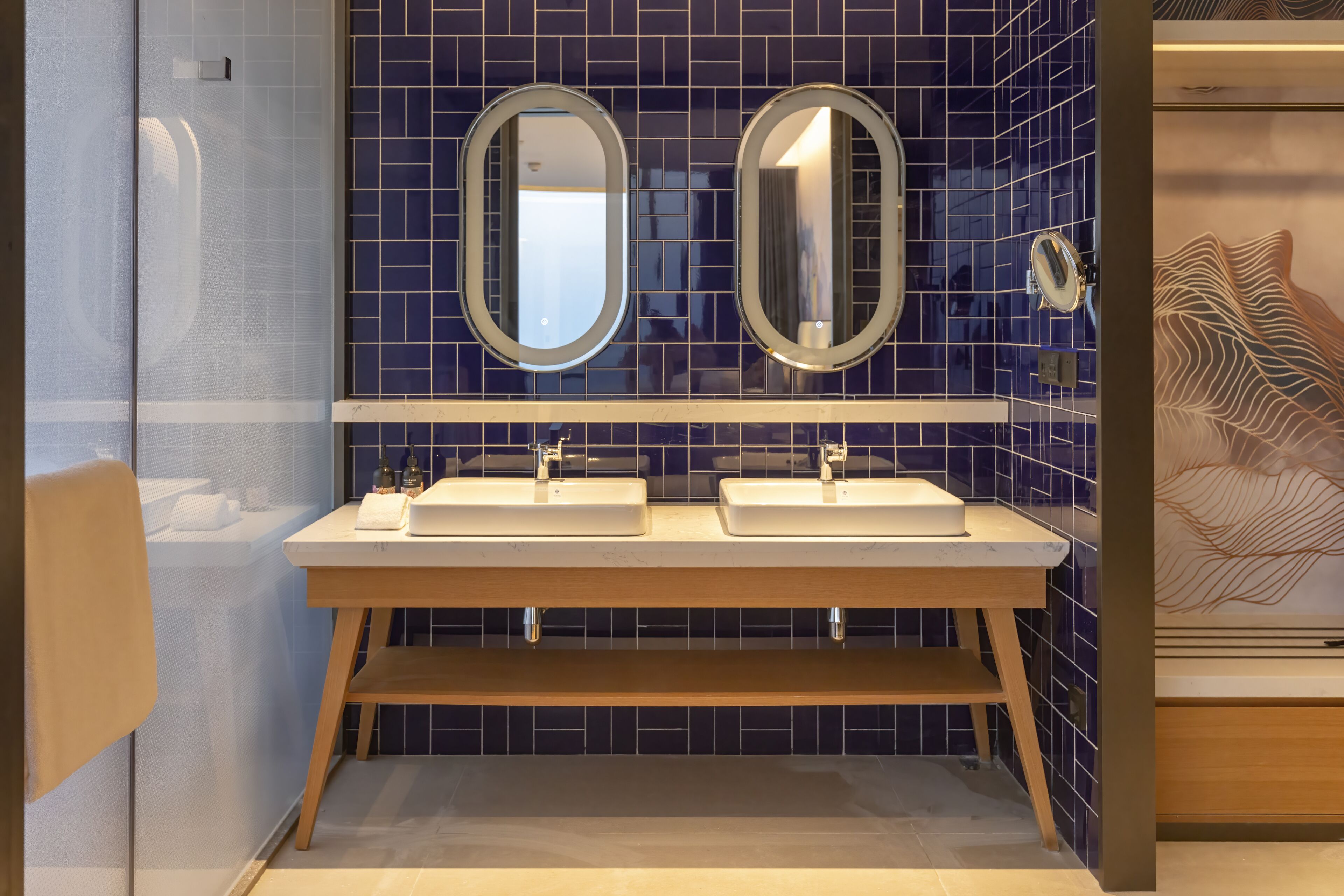 A modern bathroom with two sinks, a mirror above each, and a decorative wall piece.
