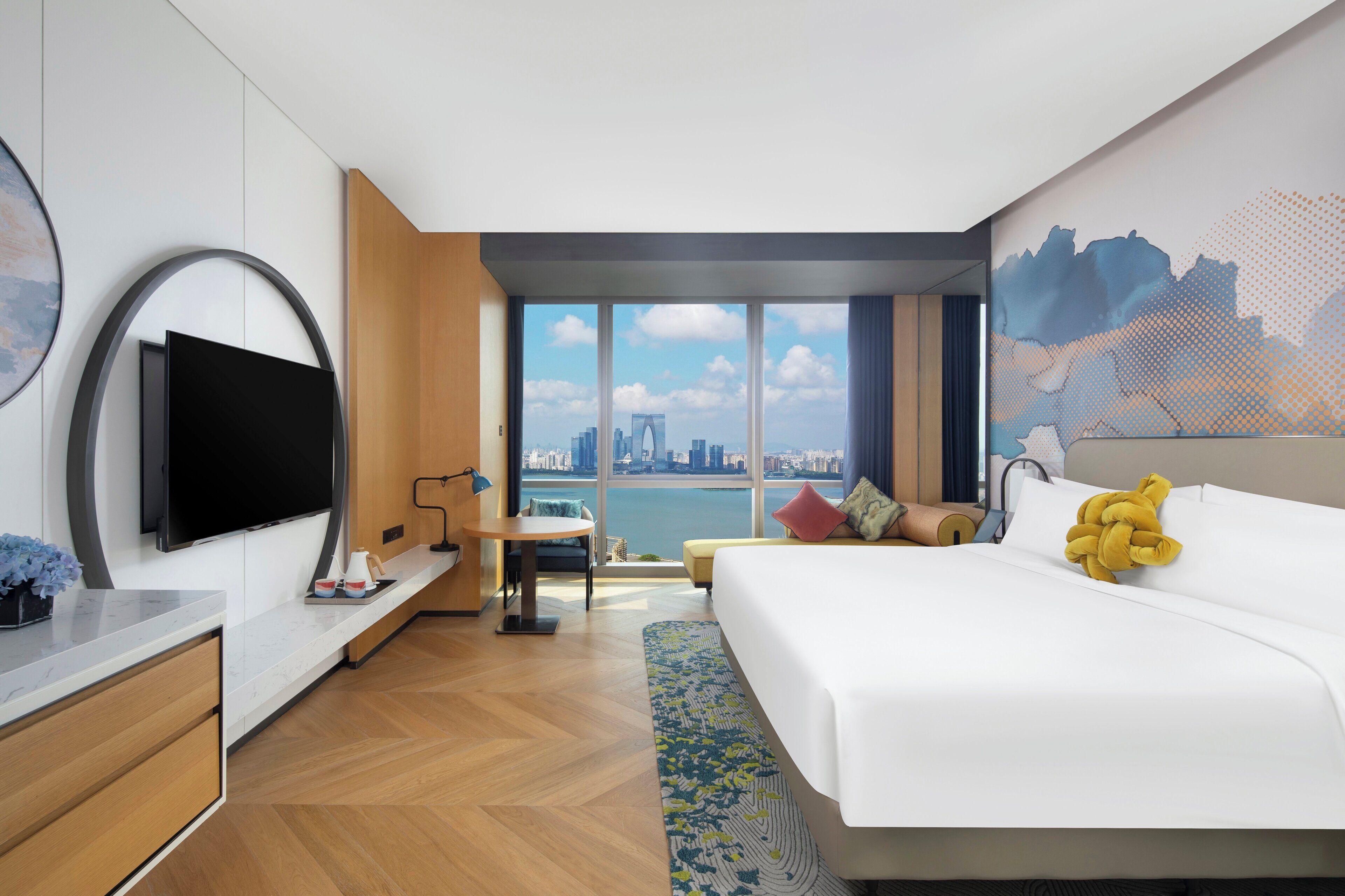 Une chambre d’hôtel moderne dotée d’un grand lit, d’une télévision à écran plat, d’un bureau et offrant une vue sur le paysage urbain.