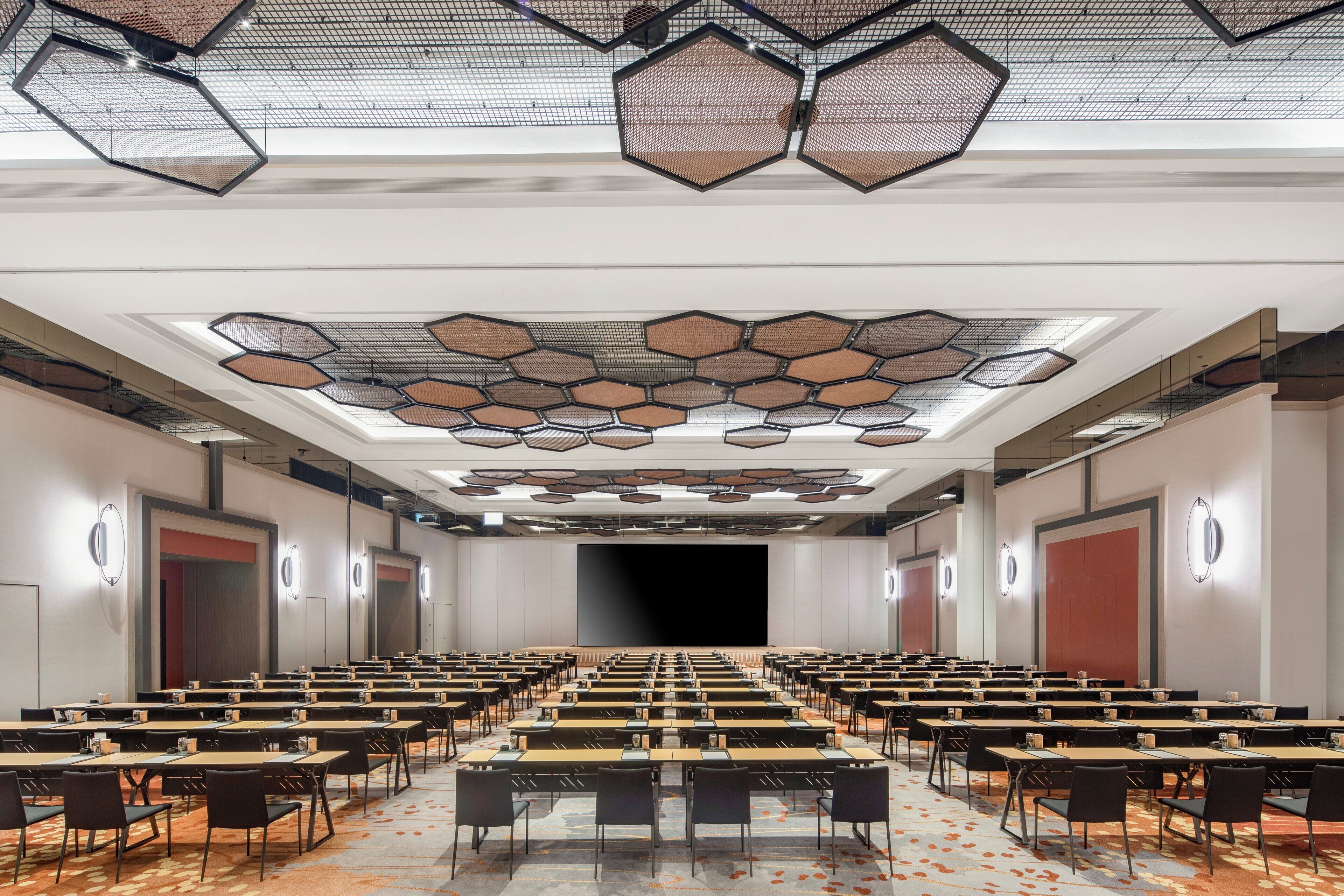 A conference room with hexagonal ceiling panels, rows of tables, and chairs.