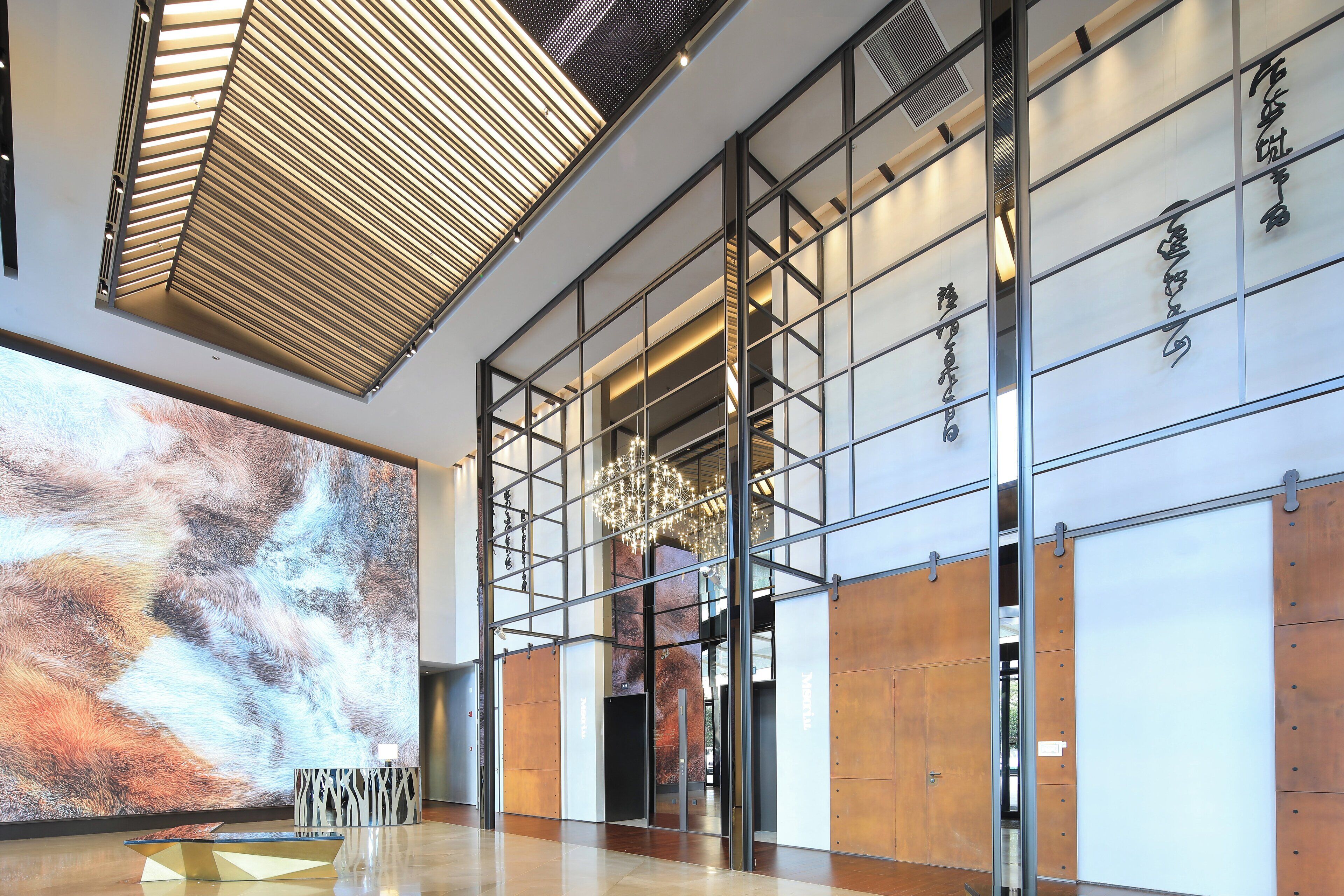 A modern lobby with a large abstract mural, a geometric glass table, and a chandelier.