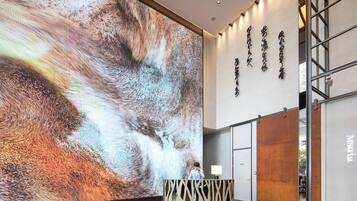 A modern hotel lobby with a large digital display, a reception desk, and a wall with text.