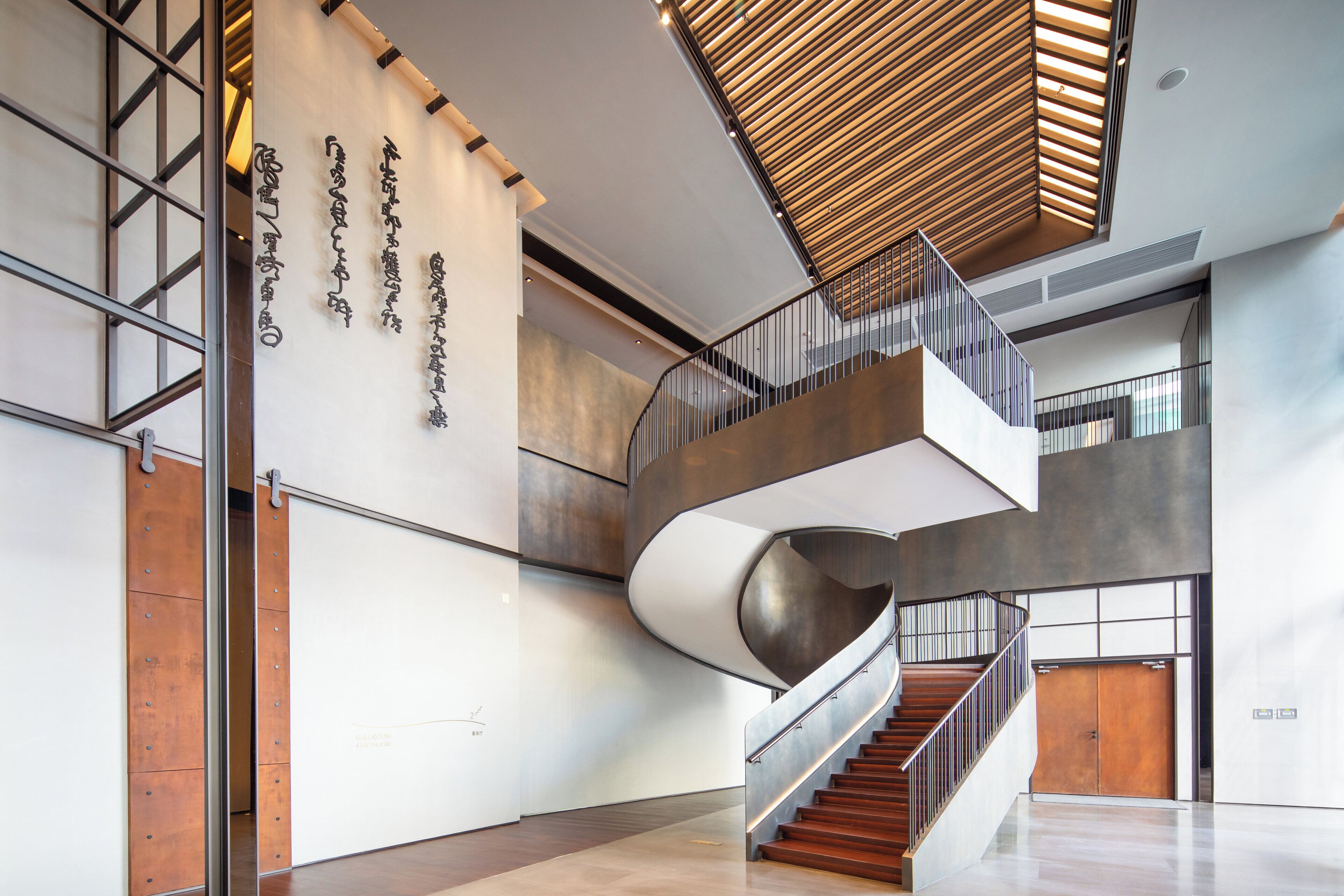 A modern interior with a spiral staircase, a wooden ceiling, and a wall with vertical text.