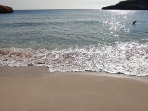 A beach with clear water, a sandy shore, and a rocky outcrop in the distance. - Marina Calas de Mallorca (Calas de Mallorca)