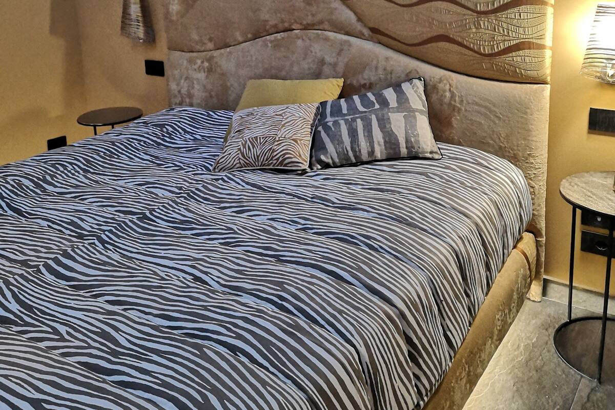 A bedroom with a bed, a headboard, a wall-mounted air conditioner, and a small table.