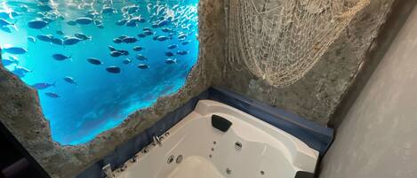 A bathtub with a view of a large aquarium filled with fish.