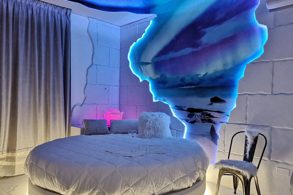 A bedroom with a bed, pillows, a chair, and a unique ceiling design.