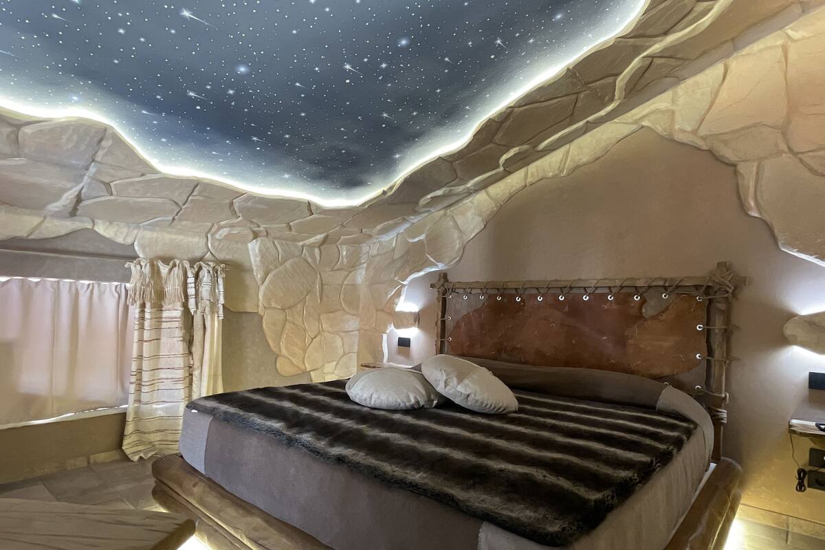 A bedroom with a stone wall, a bed with a fur blanket, and a starry ceiling.